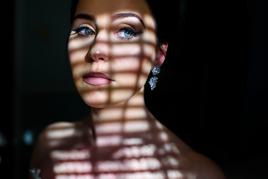 A portrait of a bride looking out the window of her family home before the wedding ceremony.